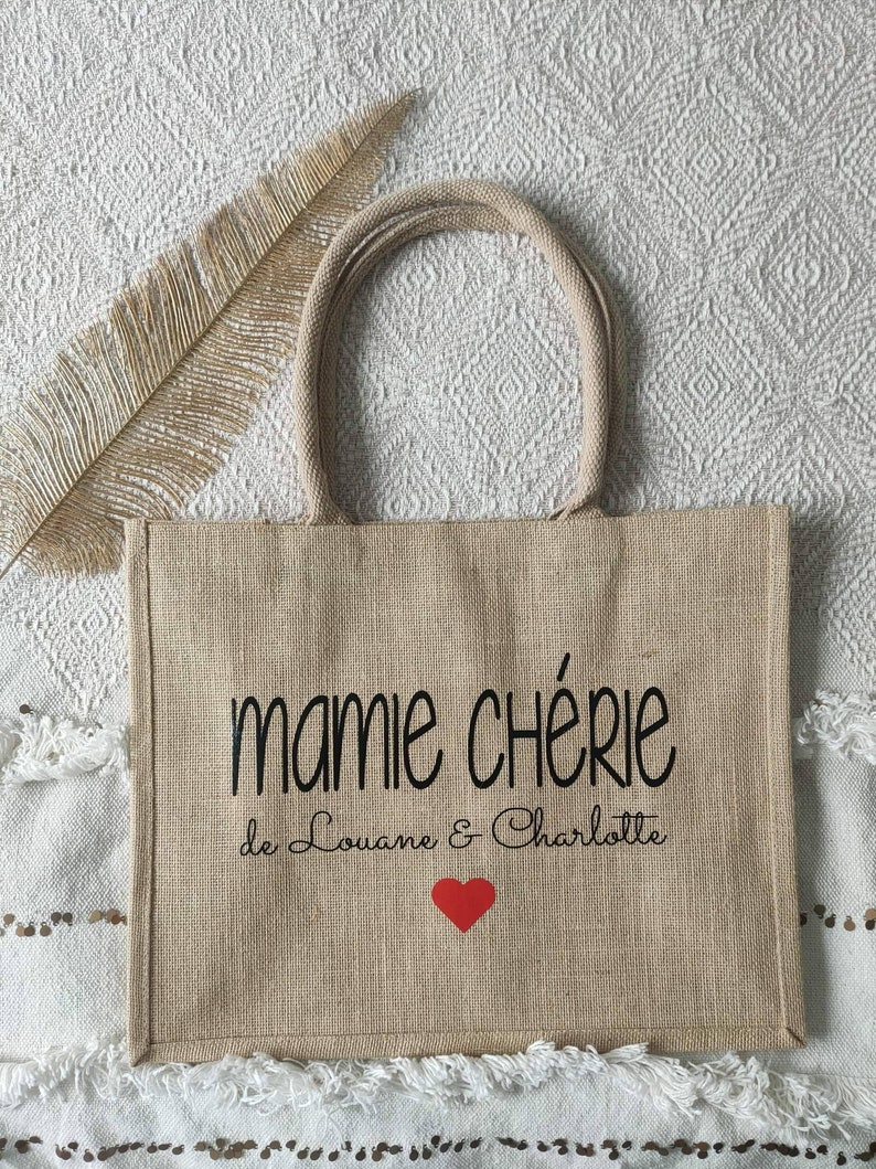 May include: A beige jute tote bag with black text that reads "mamie ch&eacute;rie de Louane & Charlotte" and a red heart.