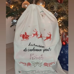 May include: A cream Christmas gift bag featuring a red Santa and reindeer design. The bag has text that reads "Delivery of gifts for Norah" and "Do not open before December 25th".