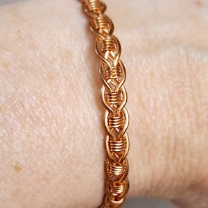 May include: A copper wire bracelet with a braided design. The bracelet is worn on a person's wrist.