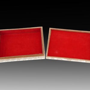 May include: Two rectangular boxes with red velvet interiors. The boxes have a light-colored, mosaic-like exterior. The boxes are open, revealing the red interior. The background is a gradient of gray and black.