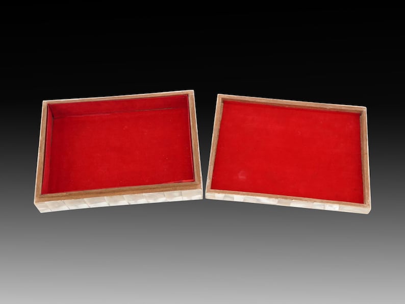 May include: Two rectangular boxes with red velvet interiors. The boxes have a light-colored, mosaic-like exterior. The boxes are open, revealing the red interior. The background is a gradient of gray and black.
