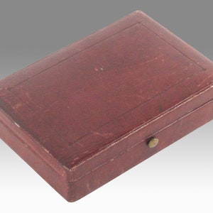 May include: A small, rectangular, red leather box with a brass clasp. The box has a raised, rectangular design on the top.
