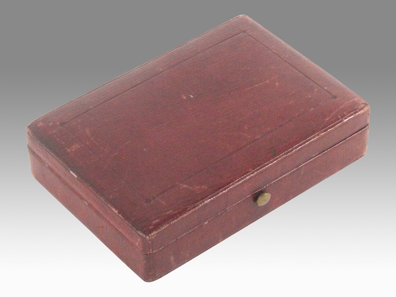 May include: A small, rectangular, red leather box with a brass clasp. The box has a raised, rectangular design on the top.