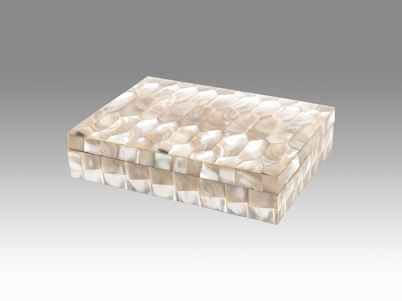 May include: Rectangular decorative box with a mother-of-pearl mosaic pattern. The box is a light cream color with a geometric design on the lid and sides. The box is a storage container.