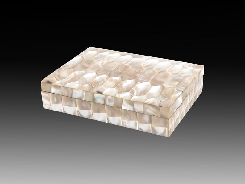 May include: Rectangular decorative box with a mother-of-pearl mosaic design. The box is white and cream-colored, with a geometric pattern on the lid and sides. The box is closed and sits on a gradient background.
