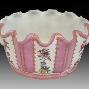 May include: A white porcelain bowl with a pink and gold floral design. The bowl has a scalloped edge and is decorated with a repeating pattern of vertical pink stripes and gold accents.