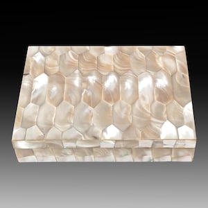 May include: A rectangular box with a lid, covered in a mosaic of iridescent, pearlescent shell pieces. The shell pieces are arranged in a repeating, geometric pattern, creating a shimmering effect. The box is likely used for storage or display.