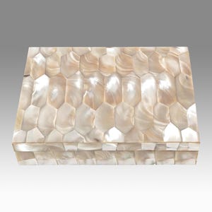May include: A rectangular box with a lid, covered in a mosaic of iridescent, cream-colored, and tan shell pieces. The shell pieces are cut into irregular, elongated hexagons, creating a textured surface. The box is likely used for storage or display.