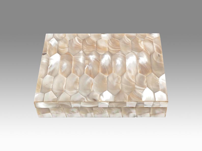 May include: A rectangular box with a lid, covered in a mosaic of iridescent, cream-colored, and tan shell pieces. The shell pieces are cut into irregular, elongated hexagons, creating a textured surface. The box is likely used for storage or display.