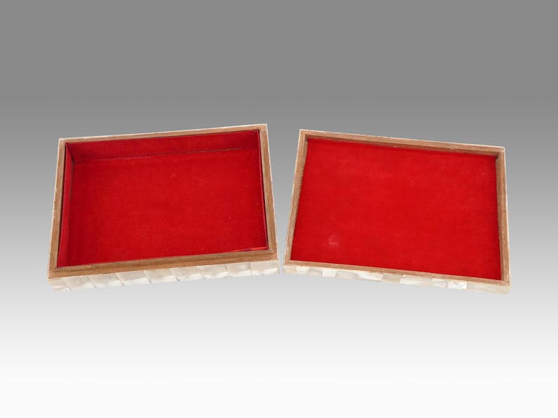May include: Open rectangular box with a red velvet interior and a mother-of-pearl exterior. The box is divided into two halves, with the lid open, revealing the red lining. The box has a wooden frame.