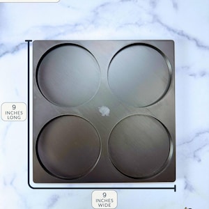 May include: A square black 3 wick candle stacker base with four circular indentations. The base measures 9 inches long and 9 inches wide. Text on the image reads: 3 WICK CANDLE STACKER BASE DIMENSIONS (APPROXIMATE), 9 INCHES LONG, 9 INCHES WIDE.