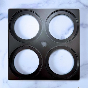 May include: A square black 3 wick candle stacker shelf with four circular cutouts arranged in a grid. The text 3 WICK CANDLE STACKER SHELF is visible in the top left corner, and a small sheep icon with the text Original Design is in the bottom right.