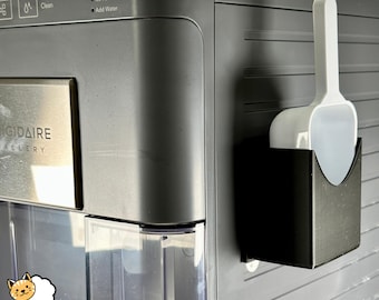 May include: A black and silver refrigerator with a white ice scoop holder attached to the side. The holder has a white scoop inside. The refrigerator has a digital display with the words "Power", "Ice Full", and "Add Water". The refrigerator also has a stainless steel panel with the words "GIGADAIRE GALLERY".