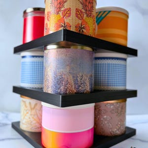 May include: A black three-tiered triangular display stand with one base and two stackers, holding nine cylindrical candles with various colourful patterns and designs. Text on the image reads 1 BASE + 2 STACKERS and CANDLES NOT INCLUDED.