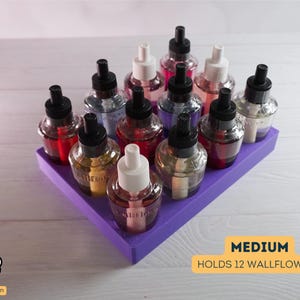 May include: A purple wallflower holder with 12 glass bottles filled with scented oil. The holder is labeled "MEDIUM HOLDS 12 WALLFLOWERS".