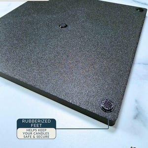 May include: A square black 3 wick candle stacker base with a textured surface. The bottom view shows four small circular rubberised feet positioned at the corners and one in the centre to provide stability for candles placed on the flat platform.