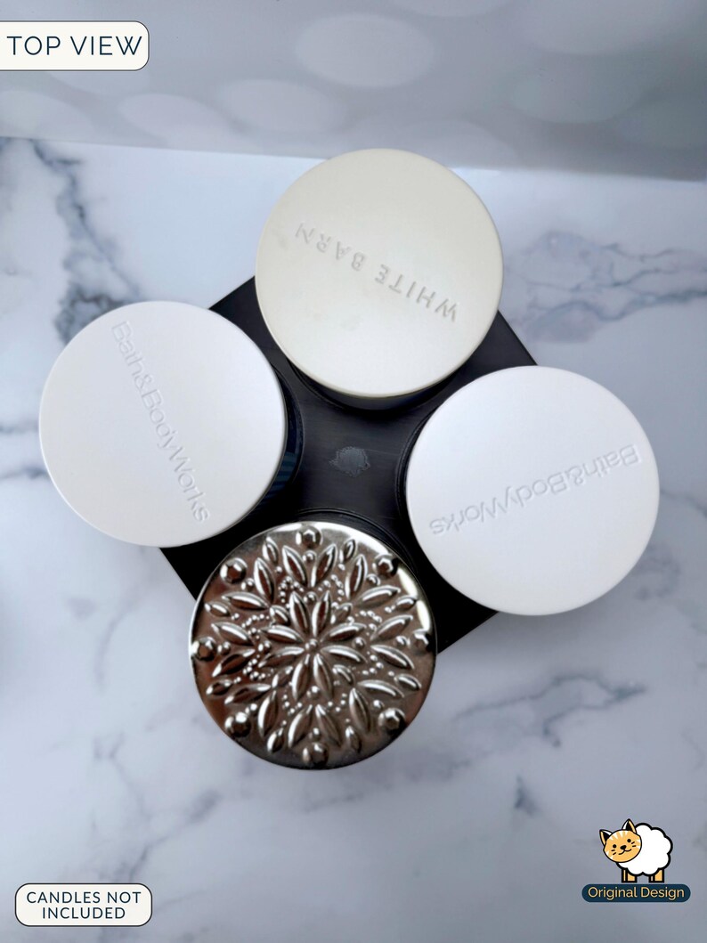May include: A black plastic candle holder with four circular slots, viewed from above. Three slots feature white lids with the embossed text Bath & Body Works or White Barn. One slot contains a silver metallic lid with a raised floral pattern.