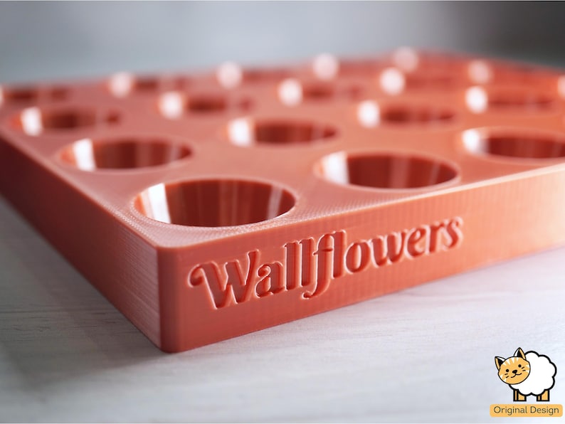 May include: A red silicone mold with 12 circular depressions, designed for making small cakes or other treats. The mold has the word "Wallflowers" embossed on the bottom.