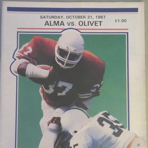 May include: A vintage football game program from Saturday, October 31, 1987, featuring Alma vs. Olivet. The cover displays a color photograph of two football players in action, one in a maroon jersey and one in white, with The College Game logo.