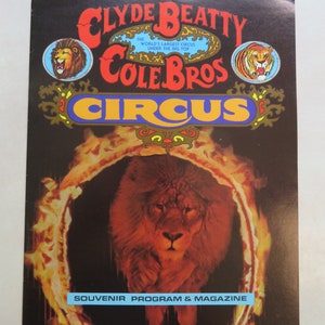 May include: A vintage souvenir program and magazine for the Clyde Beatty Cole Bros Circus. The cover features a lion walking through a fiery ring with the circus name in bold letters.