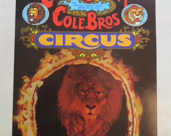 Könnte beinhalten: Ein Vintage-Souvenirprogramm und -magazin für den Clyde Beatty Cole Bros Circus. Das Cover zeigt einen Löwen, der durch einen Feuerring geht, mit dem Namen des Zirkus in fetten Buchstaben.