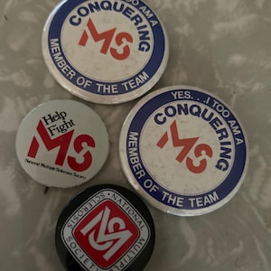 May include: Four circular pinback buttons featuring Multiple Sclerosis awareness designs. Two large buttons are white with blue text reading YES... I TOO AM A CONQUERING MEMBER OF THE TEAM and a red MS logo. One white button says Help Fight MS. One black button features a red MS logo.