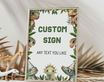 May include: A rectangular sign in a thin gold frame featuring a white background with green leaves and cartoon dinosaurs. The text reads CUSTOM SIGN in large green letters and ANY TEXT YOU LIKE in smaller black letters below the main heading.