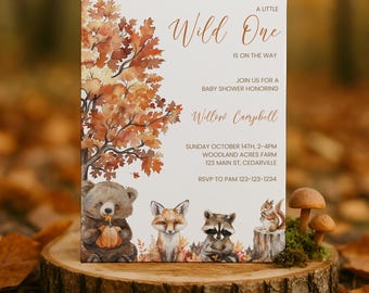 May include: A rectangular baby shower invitation card featuring a watercolour illustration of a large autumn tree with orange leaves, a bear holding a pumpkin, a fox, a raccoon, and a squirrel. The text reads A LITTLE WILD ONE IS ON THE WAY.