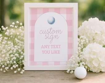 Puede incluir: Un letrero con marco blanco que presenta un fondo de cuadros vichy rosa y blanco con un panel central arqueado. El letrero muestra un gráfico de una pelota de golf azul, el texto cursivo "custom sign" y el texto "ANY TEXT YOU LIKE" en rosa.