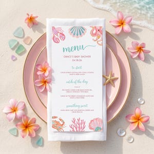 Könnte beinhalten: Eine Babyparty-Menükarte auf einer weißen Serviette, mit einem rosa Teller, Seestern und Plumeria-Blüten. Die Speisekarte hat ein Aquarelldesign von Meereskreaturen und Korallen. Die Speisekarte lautet "Grace's Baby Shower 04.28.26".