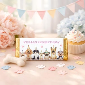 Op de afbeelding: Een verpakte chocoladereep met een aangepast etiket met de tekst "STELLA'S 2ND BIRTHDAY". Het etiket toont illustraties van honden met feesthoeden. Een cupcake, pootafdrukken en een hondenbot zijn ook zichtbaar.