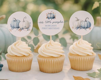 May include: Three cupcakes topped with round paper toppers featuring watercolor illustrations of blue and white pumpkins, berries, and leaves. The center topper displays the text: our little pumpkin MORGAN'S FIRST BIRTHDAY in blue script and block font.