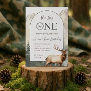 Peut inclure: Une carte d'invitation rectangulaire illustrée d'un paysage de montagnes, de forêt et d'un élan. Le texte indique : The Big ONE, JOIN US IN CELEBRATING, Hunter's First Birthday, SATURDAY NOVEMBER 3RD, 3:00-5:00PM, BIG BEAR HUNTING LODGE, 123 FOREST LANE, TORONTO, RSVP TO KASEY 123-123-1234.