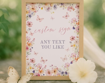 Op de afbeelding: Een rechthoekig bord in een lichthouten lijst met een bloemenrand van roze, oranje en paarse bloemen en kleine vlinders. De tekst luidt "custom sign" in een roze scriptlettertype en "ANY TEXT YOU LIKE" in een grijs schreeflettertype.