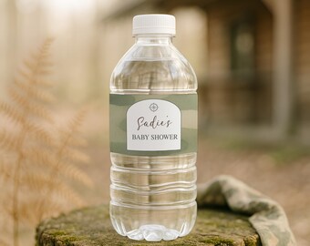 May include: A clear plastic water bottle with a white cap and a custom label featuring a sage green camouflage pattern. The label displays a compass icon above the text "Sadie's BABY SHOWER" printed in a dark, elegant serif font style.