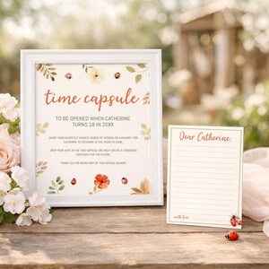 Könnte beinhalten: Ein weiß gerahmtes Schild mit dem Text time capsule to be opened when Catherine turns 18 in 20XX, verziert mit Aquarell-Marienkäfern und Blumen. Daneben liegt eine passende linierte Notizkarte mit dem Text Dear Catherine und with love.