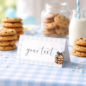 May include: A place card with a light blue and white gingham pattern, featuring the words "your text" in cursive. A stack of chocolate chip cookies with a ribbon is on the right. Cookies, a jar of cookies, and a milk bottle are in the background.