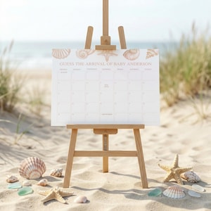 May include: A wooden easel displays a white calendar with the text "Guess the Arrival of Baby Anderson" and seashell illustrations. The calendar is on a sandy beach with seashells and starfish scattered around the easel.
