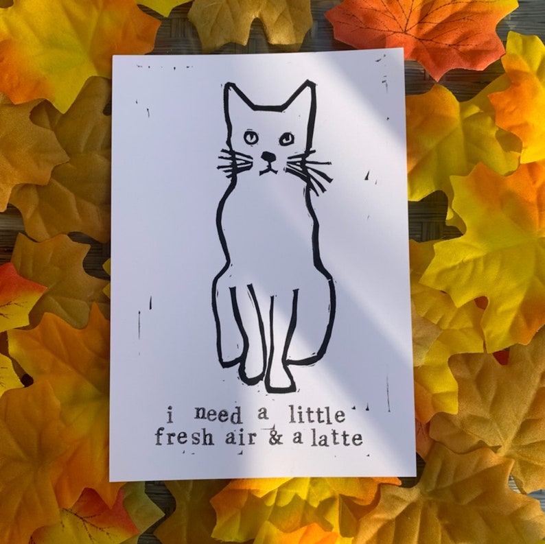 Pu&ograve; includere: Un'illustrazione in bianco e nero di un gatto seduto con il testo "i need a little fresh air & a latte." stampato sotto.