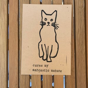 Pu&ograve; includere: Un'illustrazione in bianco e nero di un gatto seduto con il testo "curse my sarcastic nature" sotto.