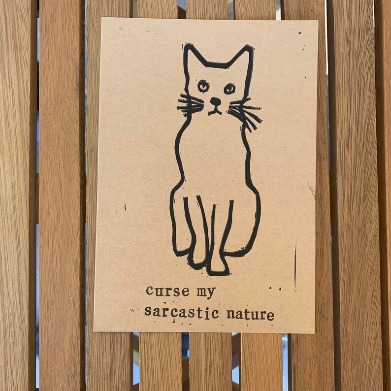 Pu&ograve; includere: Un'illustrazione in bianco e nero di un gatto seduto con il testo "curse my sarcastic nature" sotto.