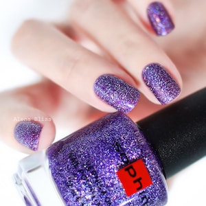 Puede incluir: Una botella de esmalte de uñas de purpurina morado con una etiqueta cuadrada roja que dice "pH". La botella está sobre una superficie blanca. Una mano con esmalte de uñas de purpurina morado está sosteniendo la botella.