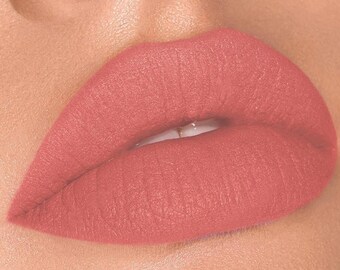 Puede incluir: Primer plano de unos labios pintados con pintalabios coral mate. El pintalabios tiene una textura suave y uniforme y un acabado suave y aterciopelado. La piel alrededor de los labios es suave y ligeramente texturizada.