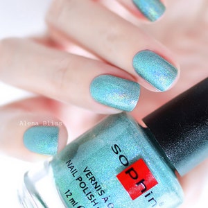 Könnte beinhalten: Nahaufnahme einer Hand mit türkisfarbenem Nagellack. Der Lack hat einen schimmernden, irisierenden Effekt. Eine Flasche Sophin Nagellack ist im Vordergrund, mit dem Text "Vernis à Ongles Nail Polish" sichtbar. Die Flasche enthält 12 ml Lack.