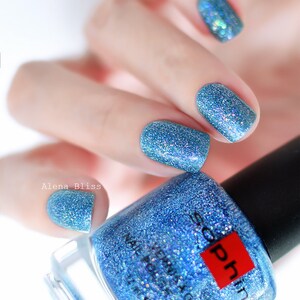 Peut inclure: Un flacon de vernis à ongles bleu pailleté avec une étiquette carrée rouge qui dit "Sophin".