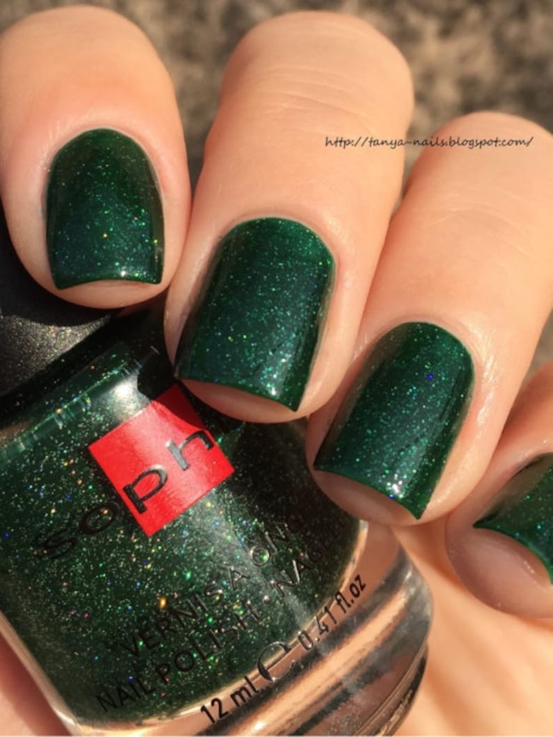 Puede incluir: Una botella de esmalte de u&ntilde;as verde oscuro con una etiqueta roja y dorada que dice "Soph" y "Vernis a Ongles Nail Polish". La botella es de 12 ml o 0.41 fl oz. El esmalte es verde oscuro con un brillo fino.