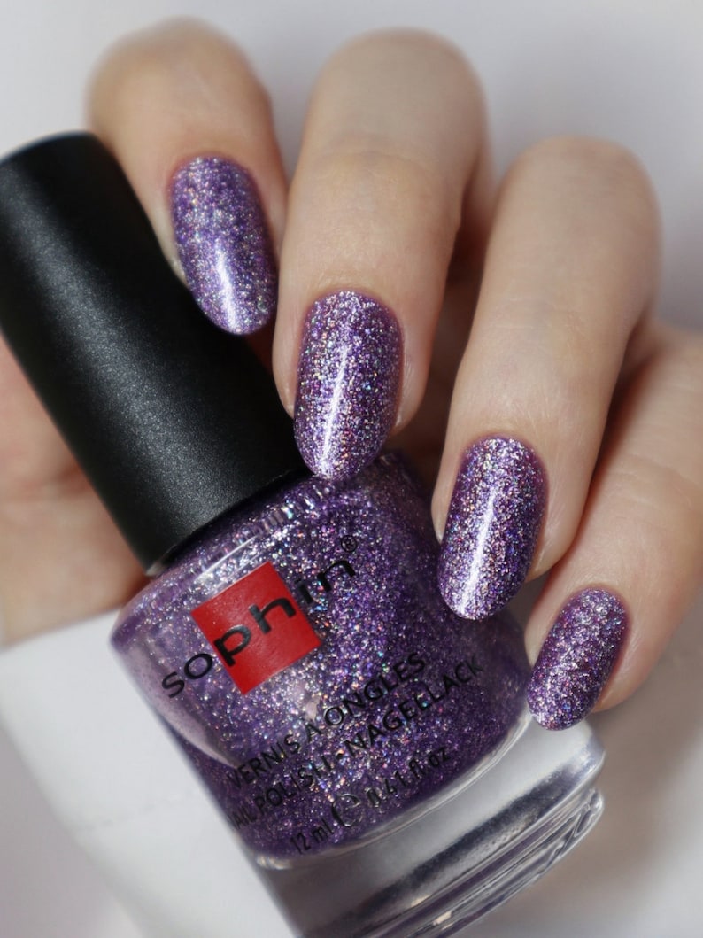 May include: A bottle of purple glitter nail polish with the brand name "Sophin" and the text "Vernis a Ongles All Polish Nail Gellack 12 ml 0.41 fl oz" on the label.