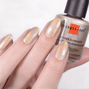 May include: A bottle of Sophiin nail polish in a shimmery gold color with a holographic finish. The bottle is labeled "Vernis &agrave; Ongles Nail Polish -  H.Nagellack 0.41 fl.oz."