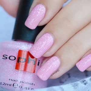 May include: Pink nail polish with a sparkly finish in a clear glass bottle with a black cap. The bottle label reads "soph" in red letters and "nail polish 12ml e 0.41 fl oz".