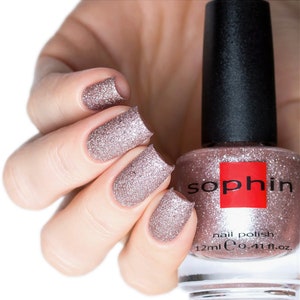 Può includere: Un flacone di smalto per unghie Sophiin di colore oro rosa scintillante con una finitura glitterata. Il flacone è da 12 ml (0,41 fl. oz.).